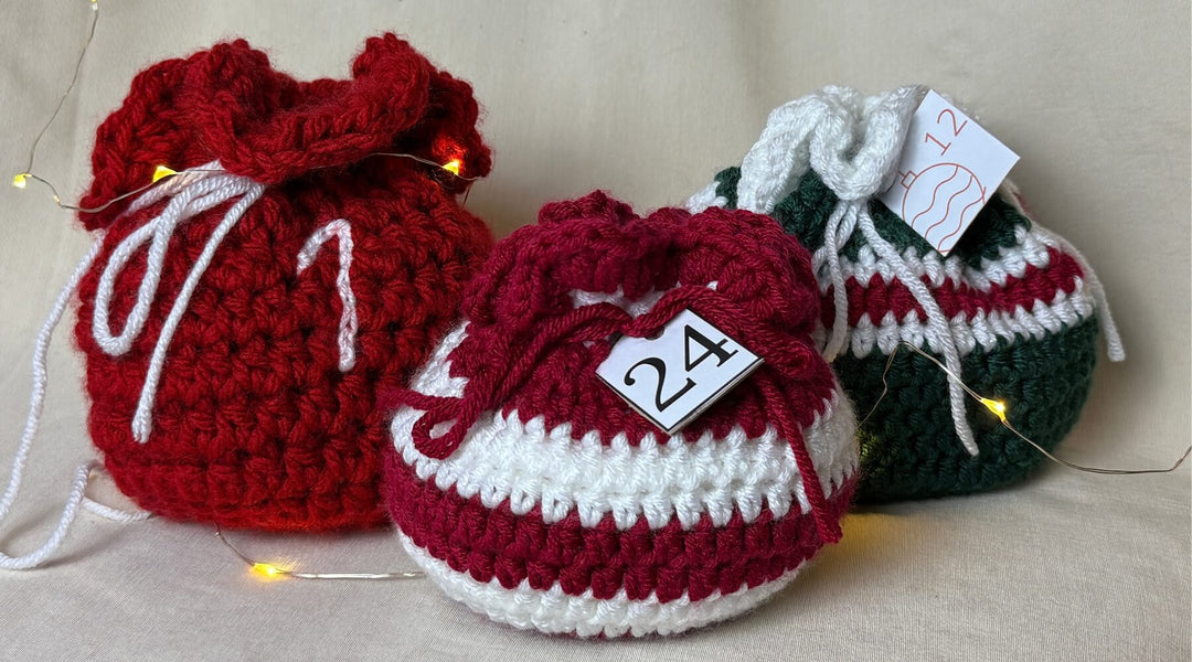 Drei farbenfrohe, gehäkelte Taschen in Rot, Weiß und Grün mit Anhängern für Adventskalender.